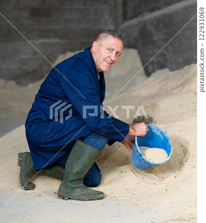 Portrait of farmer squatting at heap of corn flour 122931069