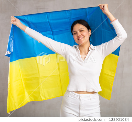 Middle-aged woman in casual clothes holds unfurled flag of Ukraine in hands raised above head Middle-aged woman in casual clothes holds unfurled flag of Ukraine in hands raised above head 122931084