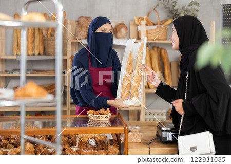 Niqab-wearing bakery worker handing baguettes to female customer 122931085