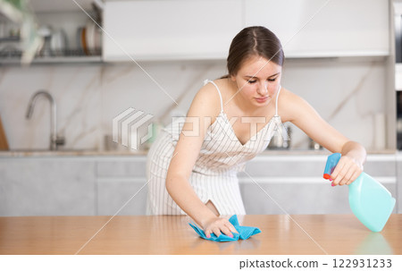 Smiling housewife with rag and detergent spray polish cleans dining table from grease and dirt Smiling housewife with rag and detergent spray polish cleans dining table from grease and dirt 122931233