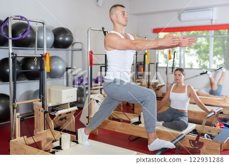 Sportive young guy training her arms and legs on reformer device 122931288