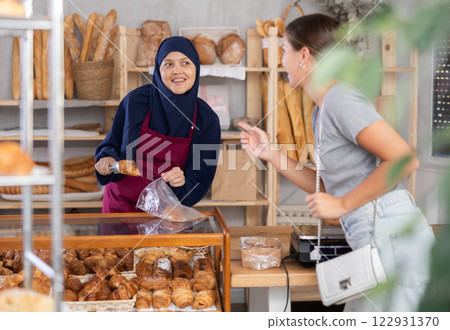 Smiling Muslim bakery worker bagging croissants for customer 122931370