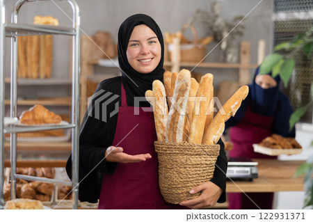 Young Muslim saleswoman displays baguettes while another seller working in background Young Muslim saleswoman displays baguettes while another seller working in background 122931371