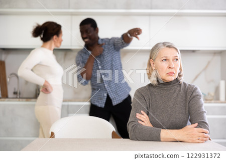 Elderly sad woman sits at table during family quarrel Elderly sad woman sits at table during family quarrel 122931372