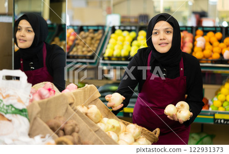 Muslim female seller in apron chooses quality onion Muslim female seller in apron chooses quality onion 122931373