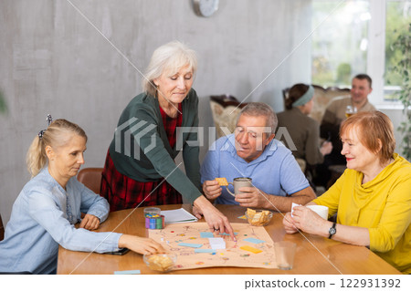 Cheerful elderly woman playing board game with friends Cheerful elderly woman playing board game with friends 122931392