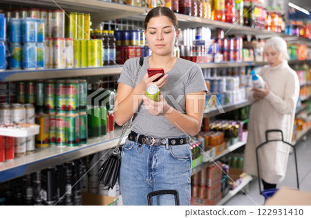Positive female customer scanning barcode on aluminum can of carbonated drink with smartphone while shopping in supermarket, paying for item using mobile app Positive female customer scanning barcode on aluminum can of carbonated drink with smartphone while shopping in supermarket, paying for item using mobile app 122931410