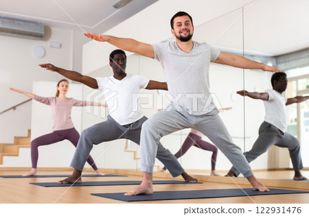 Man practising warrior two pose with group in gym 122931476