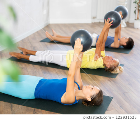 Mom, grandmother and teen grandson performing exercises with softball lying on floor Mom, grandmother and teen grandson performing exercises with softball lying on floor 122931523