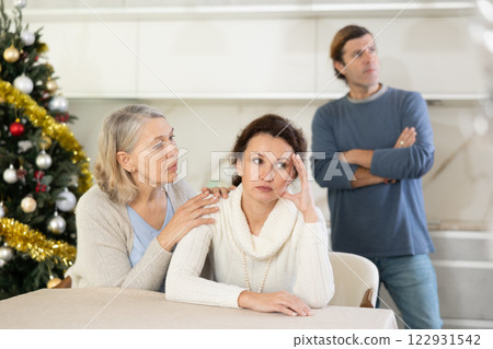 Senior woman sits near daughter and comforts during quarrel with husband on Christmas Eve Senior woman sits near daughter and comforts during quarrel with husband on Christmas Eve 122931542