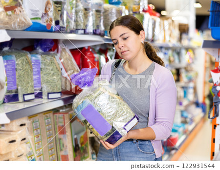 Young woman choosing straw bedding for cage of small pets in store Young woman choosing straw bedding for cage of small pets in store 122931544