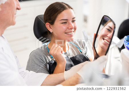 Senior man specialist holds mirror in front of girl patient and suggests evaluating effect of treatment 122931562