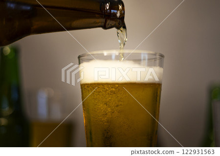 Beer is poured from the bottle into beer glass. Light fresh beer poured into glass. 122931563