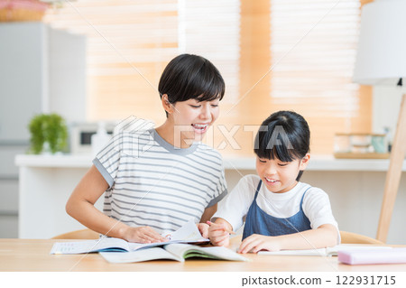 A mother stands beside her elementary school daughter as she does her homework. 122931715
