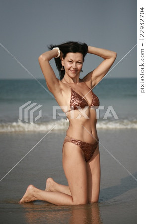 Beautiful woman 51 years old posing in Indian earrings and swimsuit with rhinestones on the sea beach in Goa India 122932704