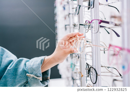 Girl hands choosing glasses in a store. Female buyer choosing glasses in a store. Female customer choosing glasses in an optical store 122932825