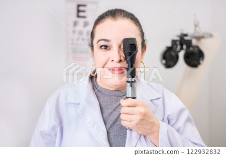 Portrait of female optometrist with ophthalmoscope in the laboratory. Smiling oculist holding an ophthalmoscope in the laboratory 122932832