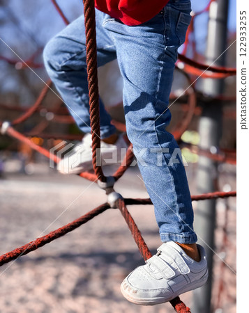 Child climbing rope structure in playground with jeans and sneakers 122933255