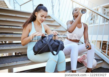 Fitness bag, water bottle and friends relax on steps with sports fashion for wellness motivation, outdoor exercise and collaboration. Healthy athlete runner couple taking break on staircase with gear 122933427