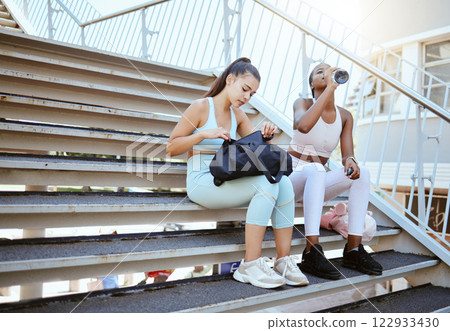 Fitness, friends relax and break on stairs after running workout together and drinking water in the outdoors. Athletic women relaxing on a stairway in exercise training for health and wellness Fitness, friends relax and break on stairs after running workout together and drinking water in the outdoors. Athletic women relaxing on a stairway in exercise training for health and wellness 122933430