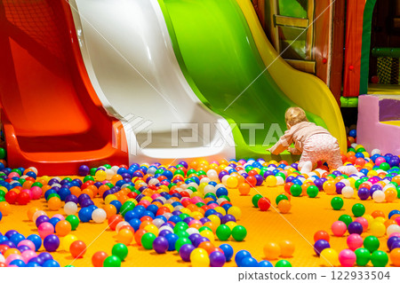 A curious toddler exploring a colorful playground with slides and a lively ball pit. 122933504
