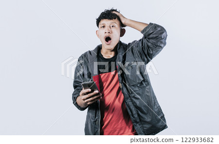 Surprised people with his cell phone holding his head, guy with cell phone shocked looking at camera, amazed man with his cell phone holding his head Surprised people with his cell phone holding his head, guy with cell phone shocked looking at camera, amazed man with his cell phone holding his head 122933682