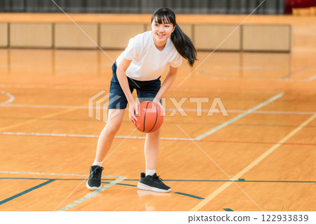 Junior high school and high school girls in gym clothes playing basketball in a gymnasium 122933839