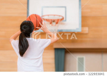 Junior high school and high school girls in gym clothes playing basketball in a gymnasium 122933841