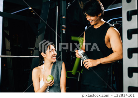 Young couple talking together after workout at gym, man hold water sport from bottle and woman holding green apple in fitness gym, eating healthy food after exercise, workout healthy lifestyle concept Young couple talking together after workout at gym, man hold water sport from bottle and woman holding green apple in fitness gym, eating healthy food after exercise, workout healthy lifestyle concept 122934101