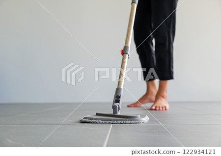Asian woman mops the floor indoors, cleaning her outdoor front home with a mop and rag. Housewife maintaining a clean home. Represents the concept of professional housekeeping and house cleanup jobs Asian woman mops the floor indoors, cleaning her outdoor front home with a mop and rag. Housewife maintaining a clean home. Represents the concept of professional housekeeping and house cleanup jobs 122934121