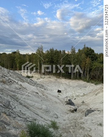 Sandy erosion with scattered rocks near forest under dynamic sky 122934725