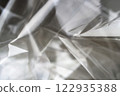 Crumpled clear plastic background, abstract glossy broken surface texture with creases 122935388