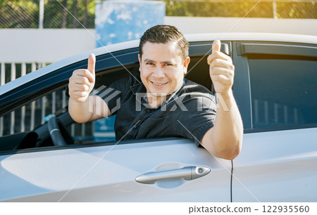 Happy driver giving a thumbs up on the road. safe driving concept. Satisfied driver man showing thumb up. Young driver man in the car showing thumb up Happy driver giving a thumbs up on the road. safe driving concept. Satisfied driver man showing thumb up. Young driver man in the car showing thumb up 122935560