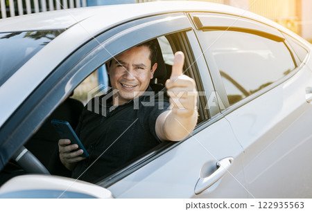 Smiling driver holding cellphone showing thumb up. Driver man showing thumb up while holding cellphone. Happy driver giving a thumbs up on the road. safe driving concept 122935563