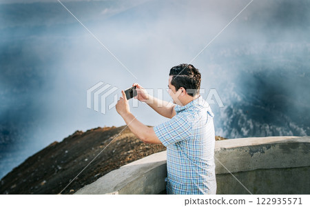 Young tourist man taking photos at a volcanic viewpoint. Adventurous man with his cell phone taking photos at a viewpoint, Tourist man taking photos at a viewpoint Young tourist man taking photos at a volcanic viewpoint. Adventurous man with his cell phone taking photos at a viewpoint, Tourist man taking photos at a viewpoint 122935571