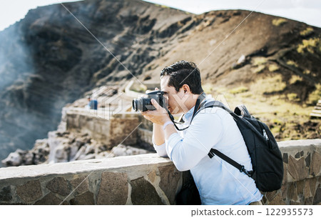 Close up of tourist man taking photos at a volcanic viewpoint. A tourist man with a photo camera taking photos at a viewpoint. Adventurous man with his camera taking photos at a viewpoint Close up of tourist man taking photos at a volcanic viewpoint. A tourist man with a photo camera taking photos at a viewpoint. Adventurous man with his camera taking photos at a viewpoint 122935573