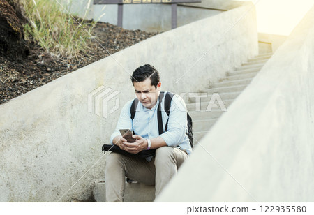 A guy sitting on stairs using his cell phone outdoors with copy space, Young man sitting on stairs using smart phone, Close up of young man sitting on stairs texting on cell phone outdoors 122935580