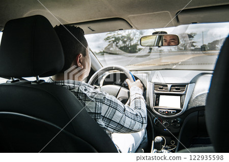 Back view of a man driving a car, Man's hands on the wheel of the car, inside view of a man driving a car, Concept of hands on the wheel of a car 122935598