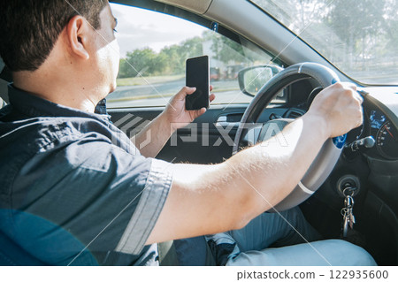 Person holding the cell phone and with the other hand the steering wheel, Man using his phone while driving, Concept of irresponsible driving, Distracted driver using the cell phone while driving Person holding the cell phone and with the other hand the steering wheel, Man using his phone while driving, Concept of irresponsible driving, Distracted driver using the cell phone while driving 122935600