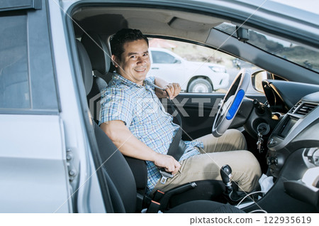 Smiling male driver putting on his seat belt. Concept of a driver in his car putting on his seat belt. Smiling person putting on seat belt, Happy driver putting on his seat belt 122935619