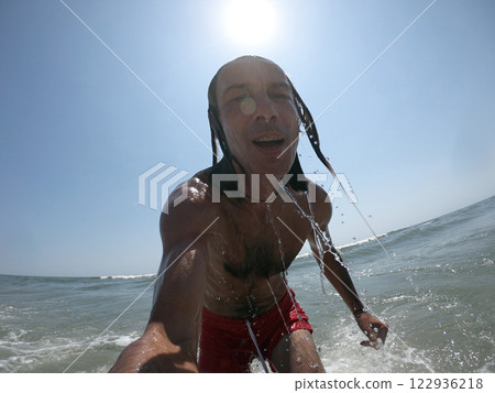 Handsome guy with long hair having fun at beach, sea waves splashing on his body 122936218