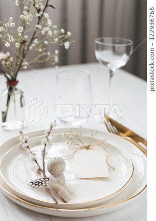 Easter table setting with willow twigs, quail eggs and tag. Golden cutlery and golden rim plates. 122936768