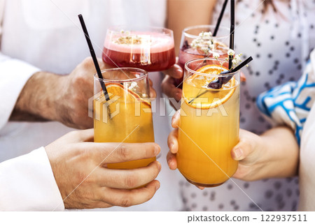 Close-up of male and female hands with elegant glasses. Men and women toast with goblets of colorful cocktails Close-up of male and female hands with elegant glasses. Men and women toast with goblets of colorful cocktails 122937511