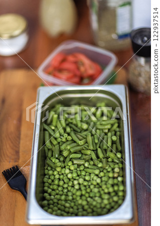 Cooking a healthy vegetarian dish. A metal bowl with fresh green peas on a wooden table. Ingredients for a delicious lunch. 122937514
