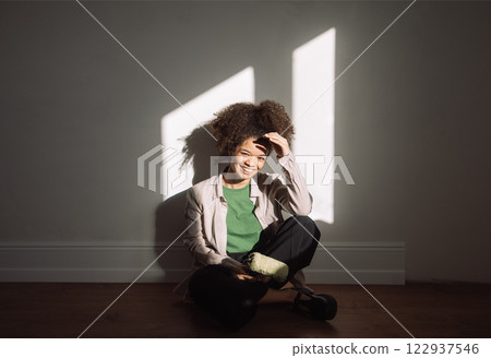 Funny girl of mixed race sits cross-legged on floorwith roller for painting walls Funny girl of mixed race sits cross-legged on floorwith roller for painting walls 122937546