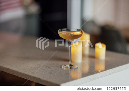 Elegant glass on a long stem with sparkling wine and lighted candles. A goblet of cool champagne on a marble countertop. 122937555