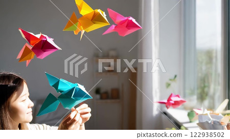 Woman playing with colorful origami birds in her bedroom Woman playing with colorful origami birds in her bedroom 122938502