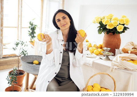 A charming girl is sitting at a table and holding lemons. A young pregnant woman in a green satin dress and shirt is dining in a rustic vintage interior. 122939994