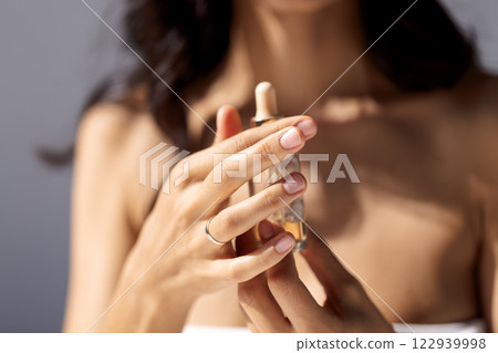 Close-up of young woman hands with natural well-groomed manicure holding bottle of moisturizing serum. Mock-up of bottle of essence with hyaluronic acid in female palms. Skin care. Close-up of young woman hands with natural well-groomed manicure holding bottle of moisturizing serum. Mock-up of bottle of essence with hyaluronic acid in female palms. Skin care. 122939998