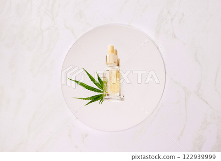 Mockup bottle cosmetic product with pipette and cannabis leaves on round mirror. Moisturizing facial serum with hyaluronic acid and hemp leaf on marble table. 122939999